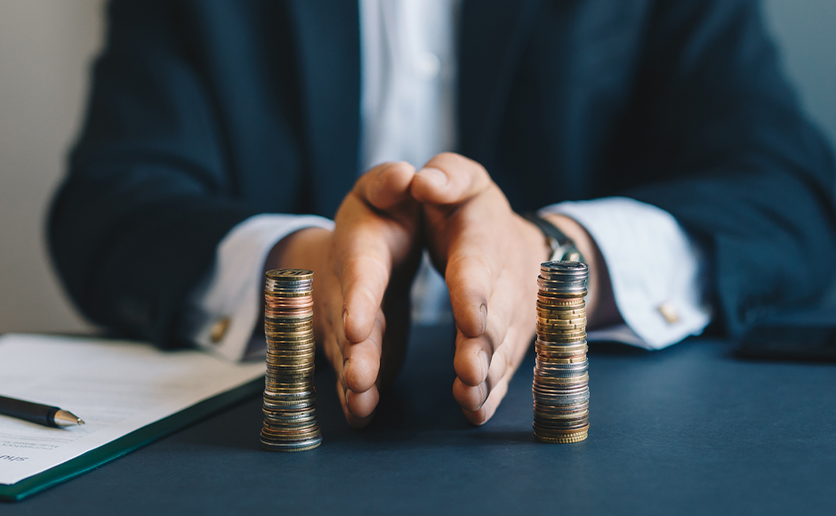 A person in a suit divides two stacks of coins on a table with cupped hands, symbolizing money management and financial planning.